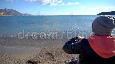坐在海滩上的女孩的后景。 在水里<strong>扔石头</strong>的女孩